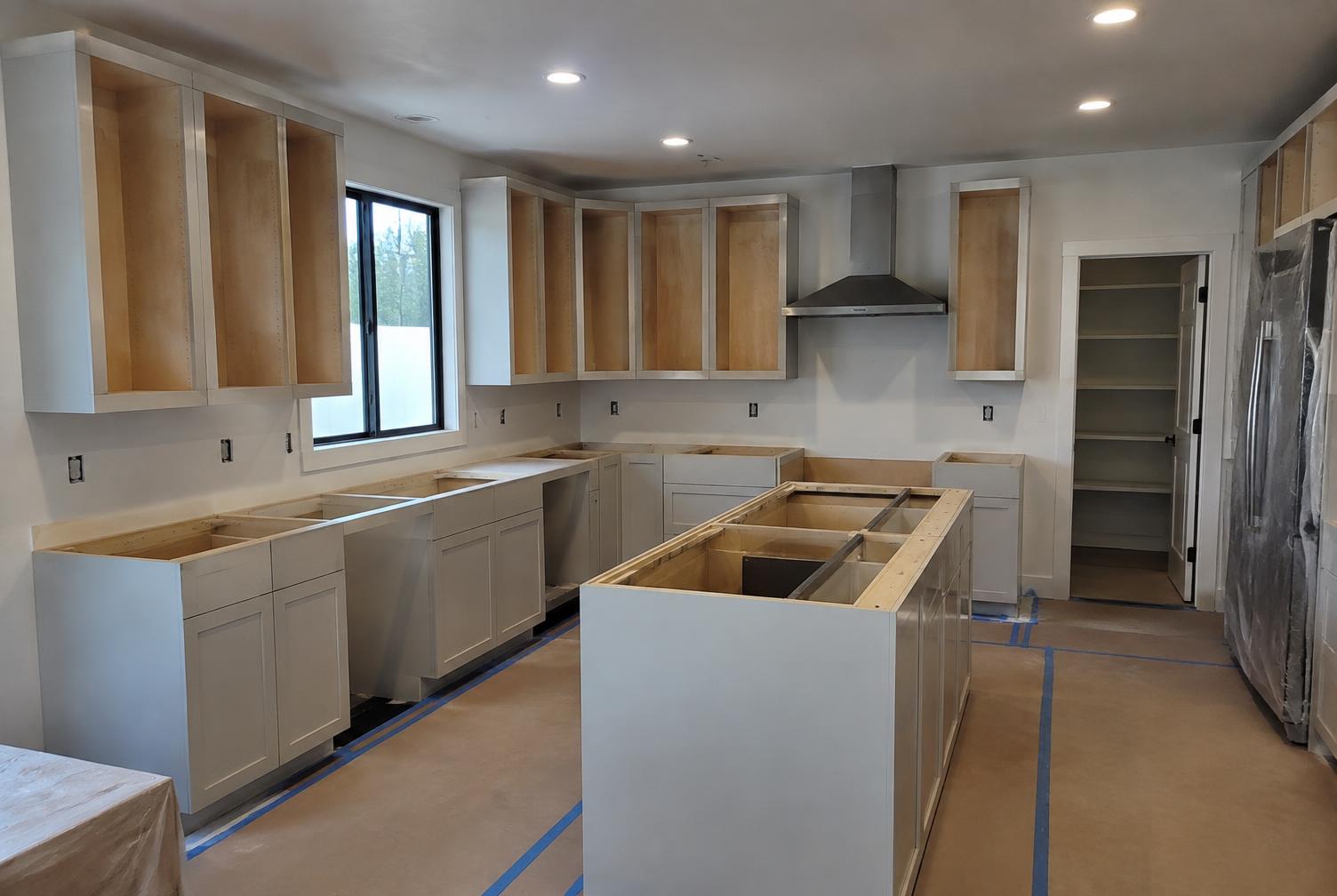 Kitchen cabinet installation in progress with protected flooring and installed cabinet boxes